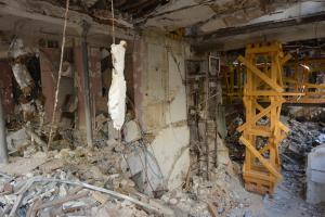 Intérieur d'un bâtiment fortement endommagé avec des débris éparpillés et des restes de supports structurels visibles.