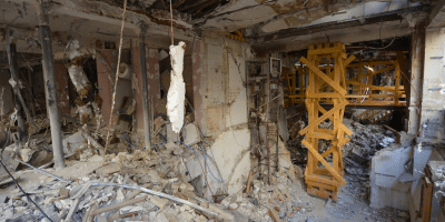 Intérieur d'un bâtiment fortement endommagé avec des débris éparpillés et des restes de supports structurels visibles.