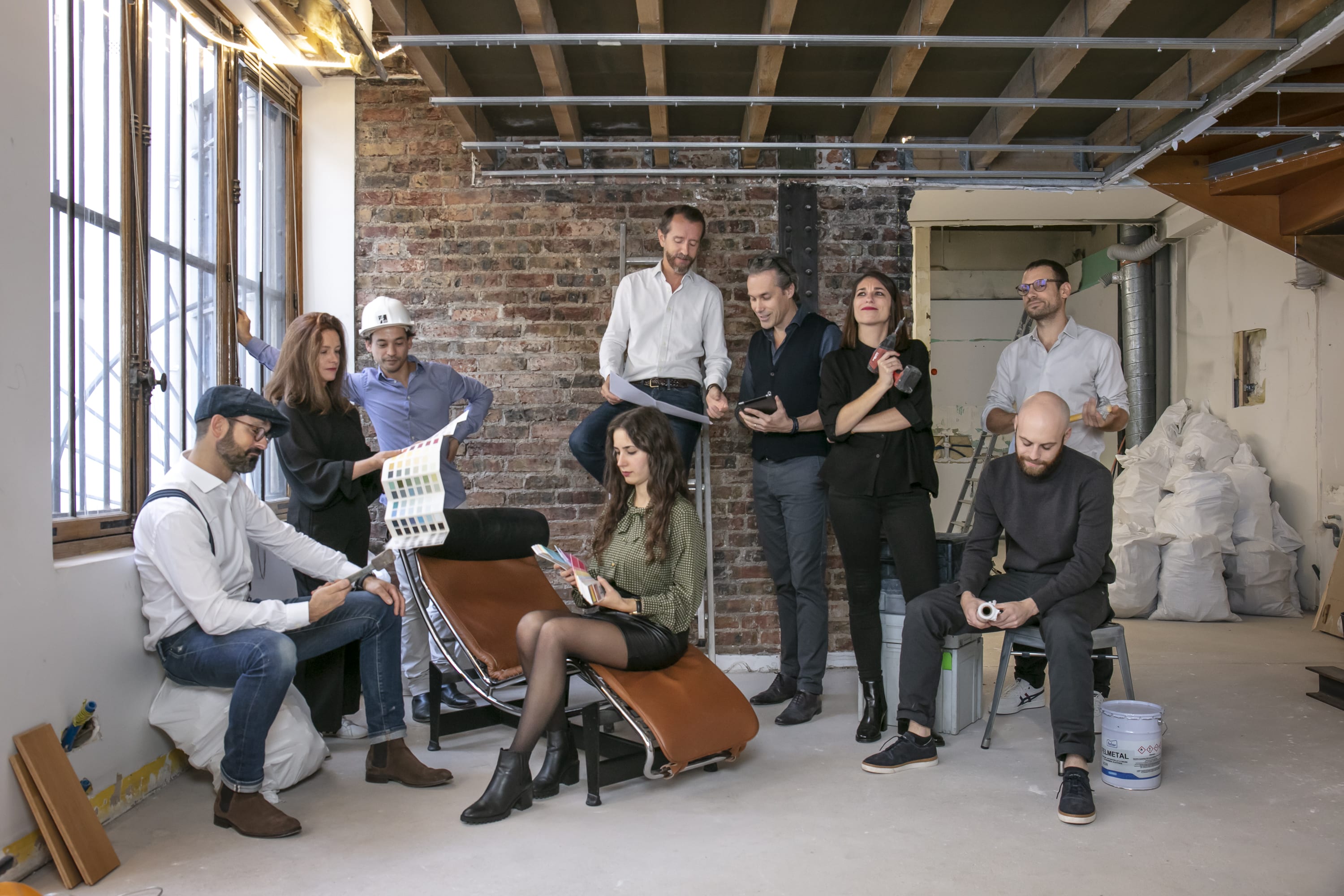 Un groupe de personnes dans une pièce partiellement rénovée, examinant des échantillons de couleurs et discutant des plans d'architecture avec leur agence.