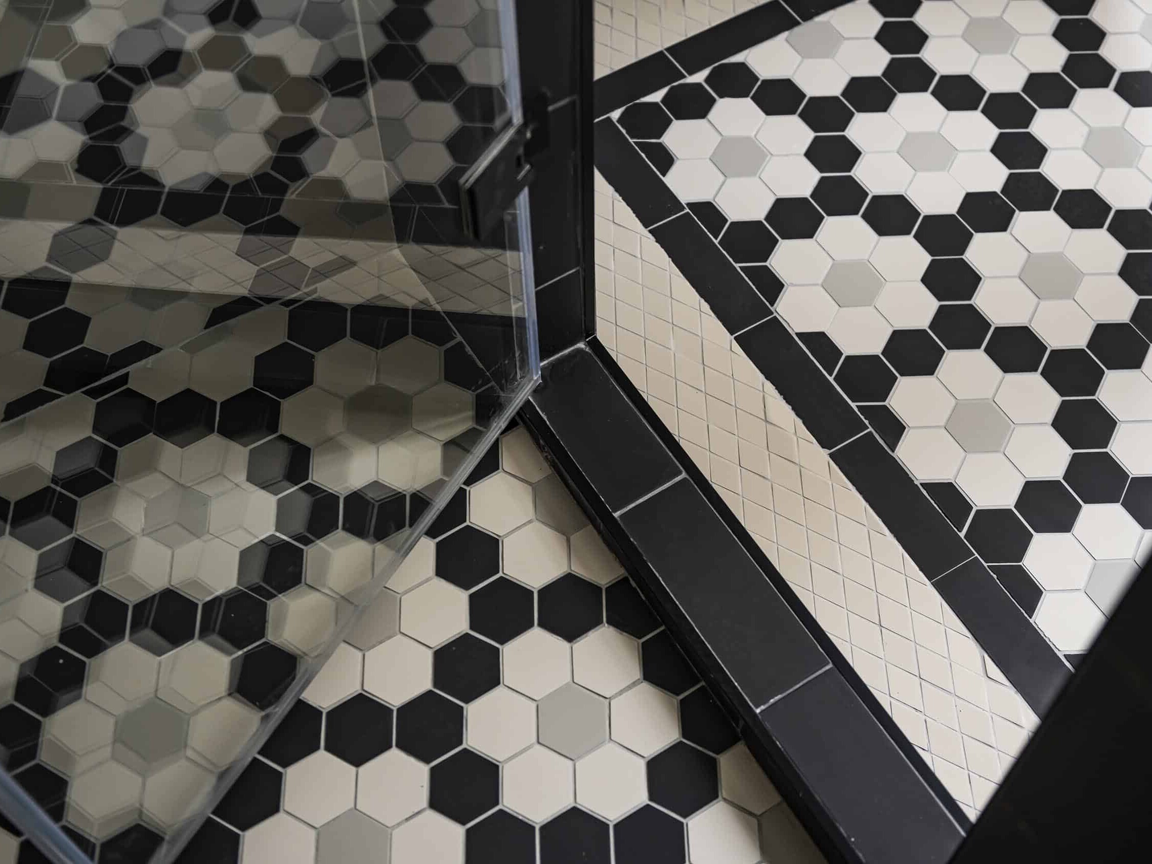 Le sol en carrelage hexagonal noir et blanc au motif géométrique complète élégamment la porte de douche en verre sans cadre, ajoutant une touche de charme haussmannien à la salle de bain.