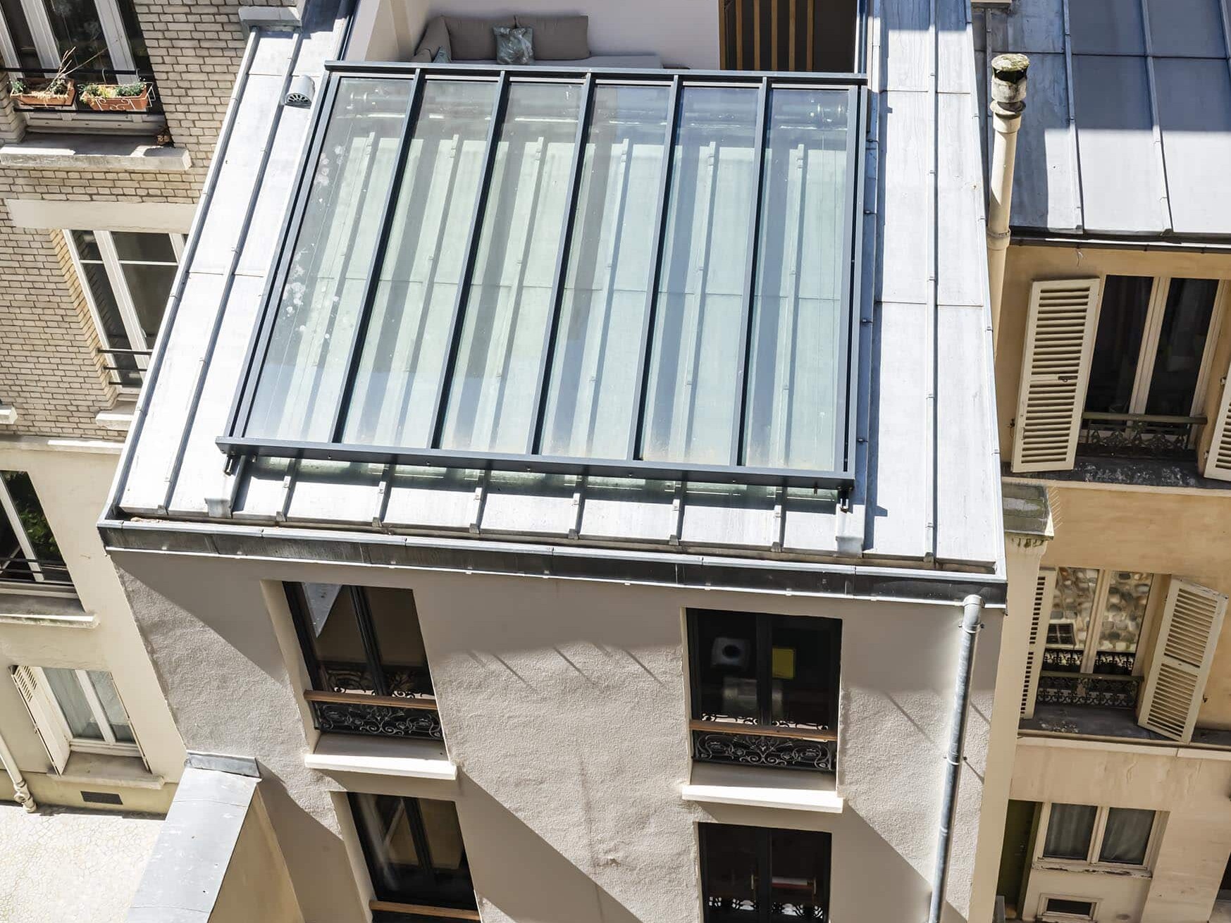 Vue aérienne d'un bâtiment moderne avec une grande section de toit en verre entourée de structures voisines plus anciennes dans une cour étroite.
