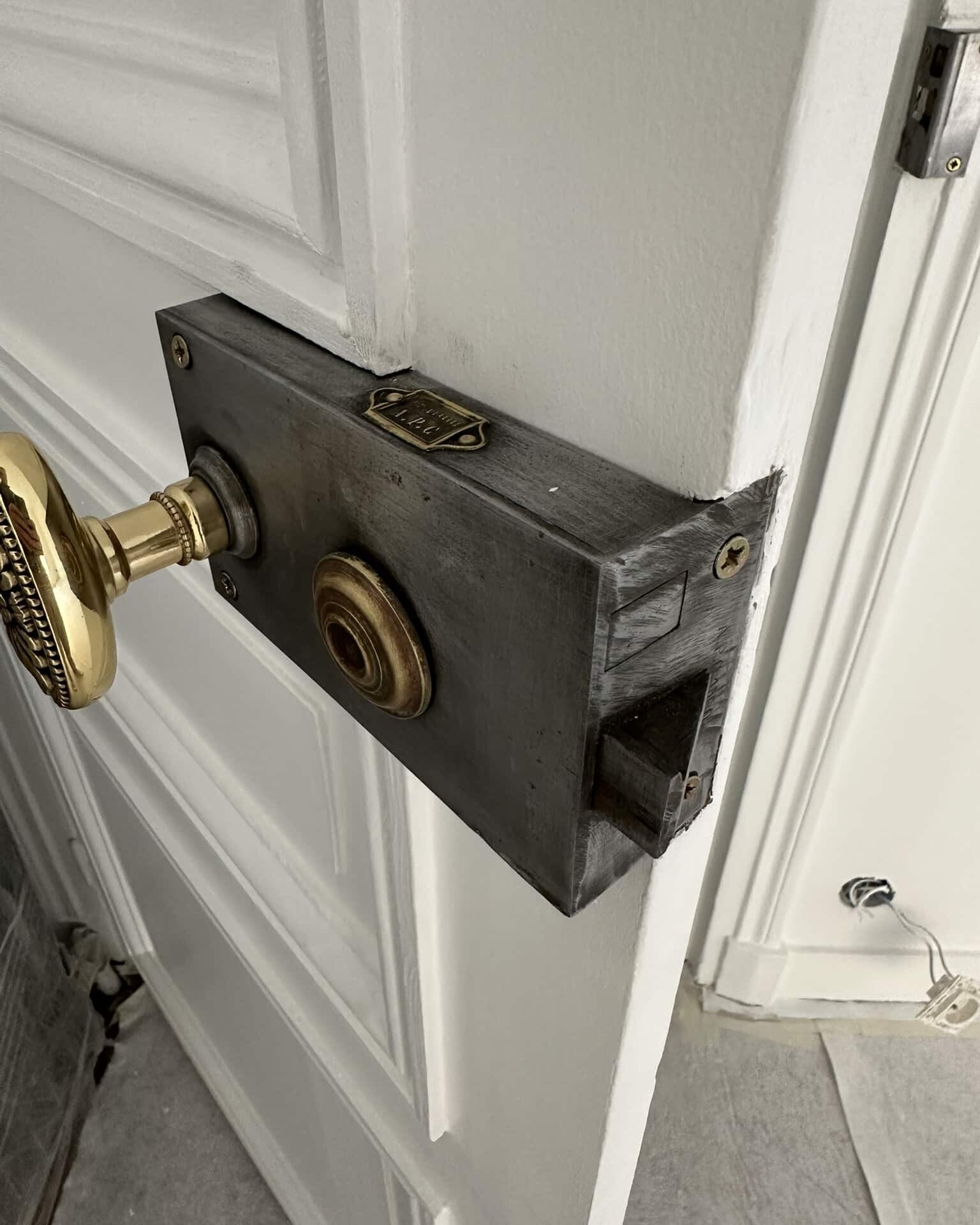 Gros plan d'une porte blanche partiellement ouverte avec une serrure de porte métallique vintage et une poignée en laiton, montrant le mécanisme de verrouillage.