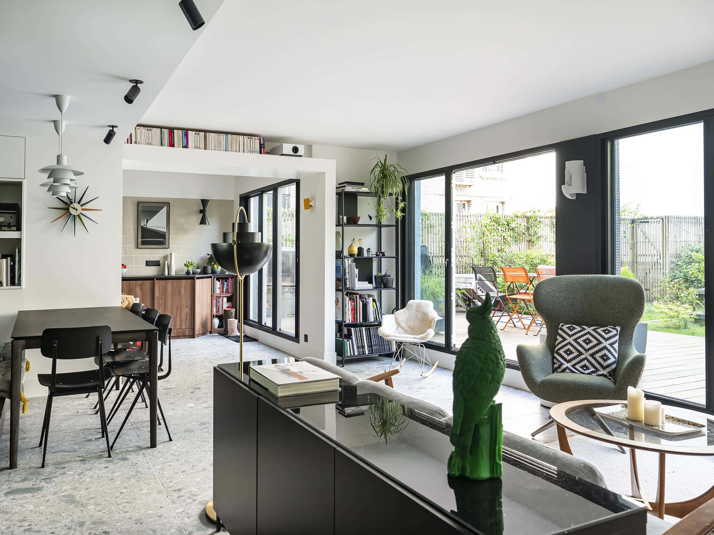 Salon et salle à manger modernes et ouverts, avec de grandes fenêtres, un mobilier minimaliste, des plantes d'intérieur et un accès à un patio avec des sièges extérieurs.