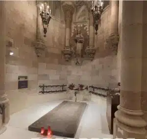 Un tombeau de pierre se trouve au centre d'une chapelle circulaire avec des colonnes, une statue ornée, des bougies et des lustres sur les murs, évoquant la riche histoire de Paris comme si elle avait été capturée sur une photo ancienne.