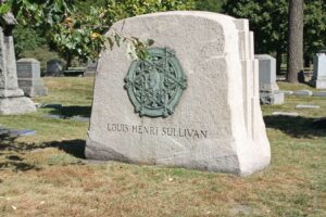 Une pierre tombale portant l'inscription "Louis Henri Sullivan", avec un relief circulaire orné, se dresse dans un cimetière avec des arbres et d'autres pierres tombales en arrière-plan, évoquant l'ambiance d'une photo ancienne et des échos de l'histoire parisienne.