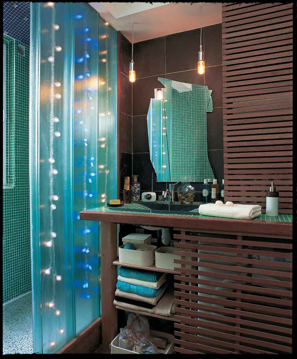 Salle de bains moderne avec cabine de douche turquoise dotée de lumières encastrées, d'un meuble en lattes de bois, d'étagères ouvertes avec des serviettes et d'un miroir brisé au-dessus d'un comptoir en carreaux de faïence.
