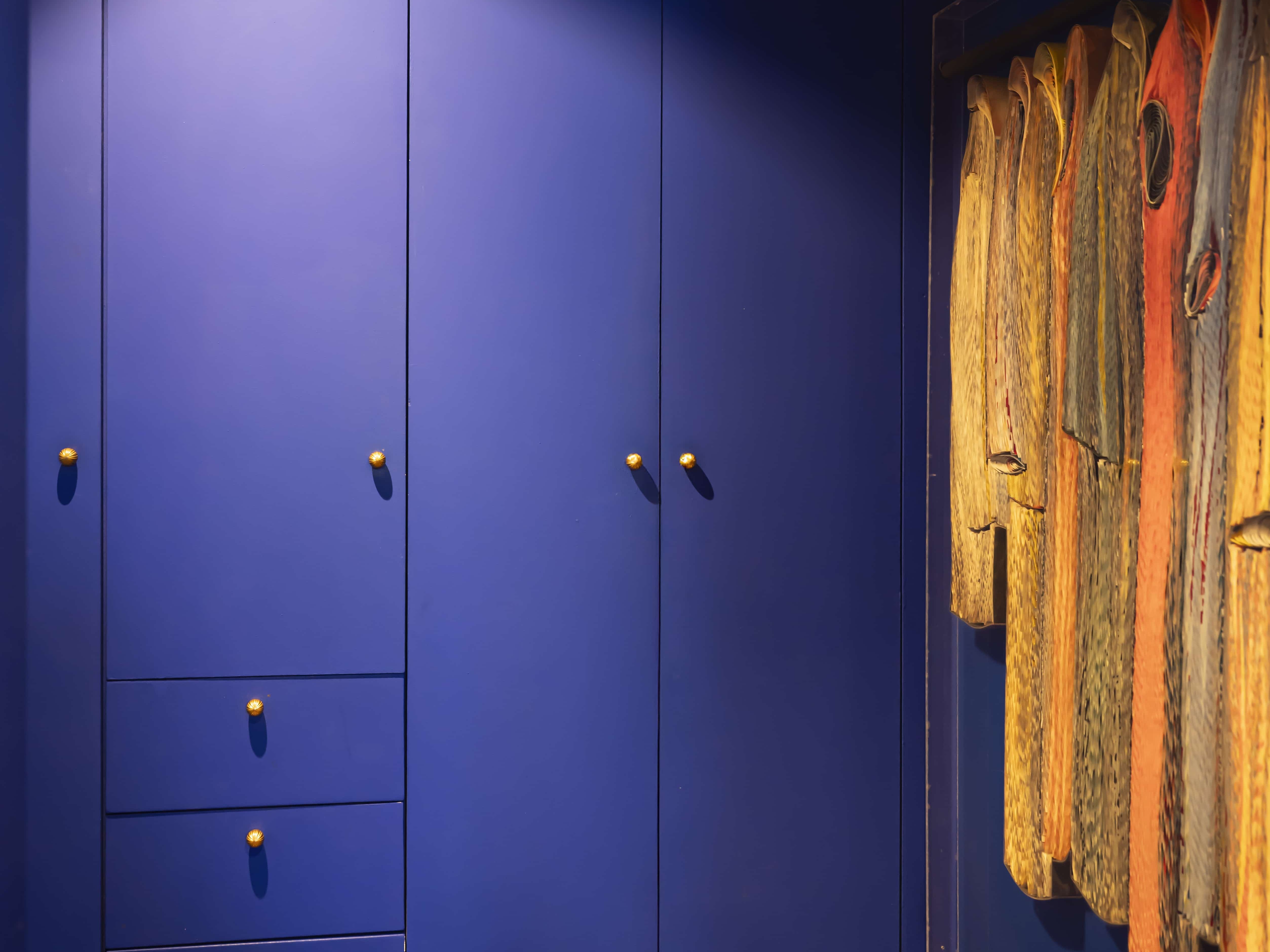 Une armoire bleue aux poignées dorées côtoie un étalage de manteaux suspendus dans une vitrine sur le sol en bois, apportant un charme haussmannien à cet appartement familial.