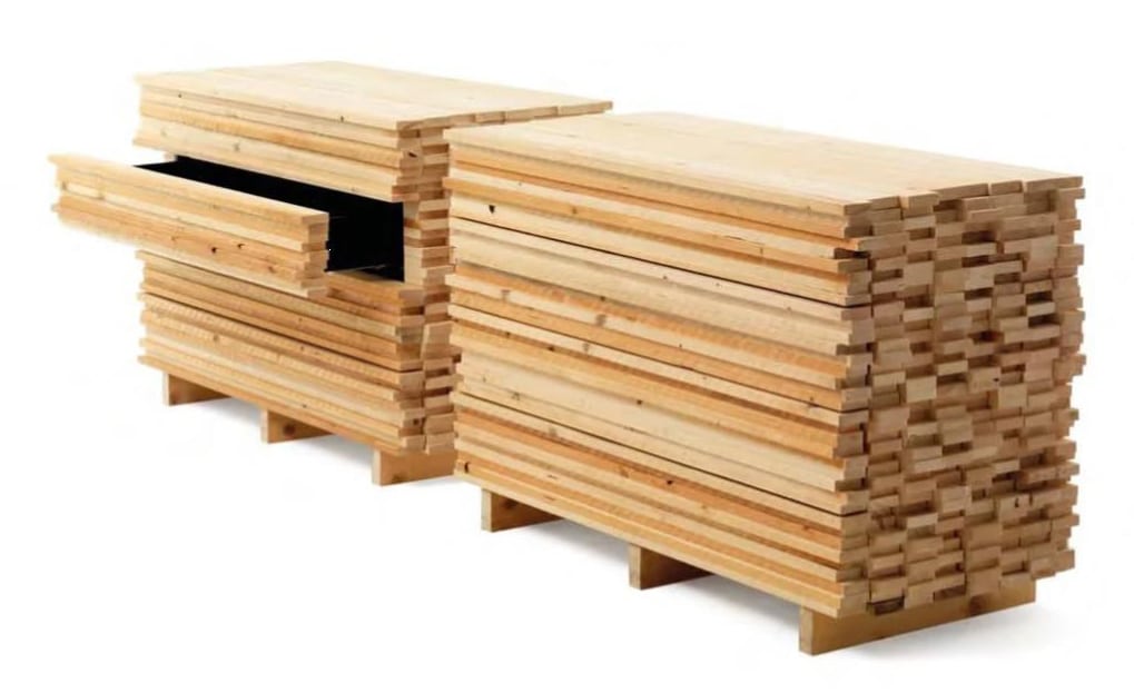 Deux piles de planches de bois sont disposées sur des palettes ; les tiroirs de l'une d'elles sont partiellement sortis, révélant des compartiments de stockage à l'intérieur.