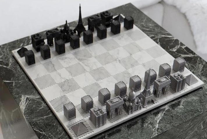 Un échiquier avec des pièces en forme de bâtiments et de monuments parisiens célèbres, placé sur une table carrée en marbre.