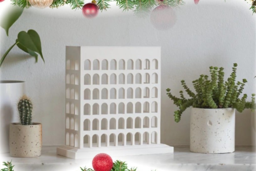 Une table avec des plantes en pot et un bâtiment décoratif blanc est encadrée par des branches de pin festives, des nœuds rouges, des boules et des pommes de pin en haut et en bas.