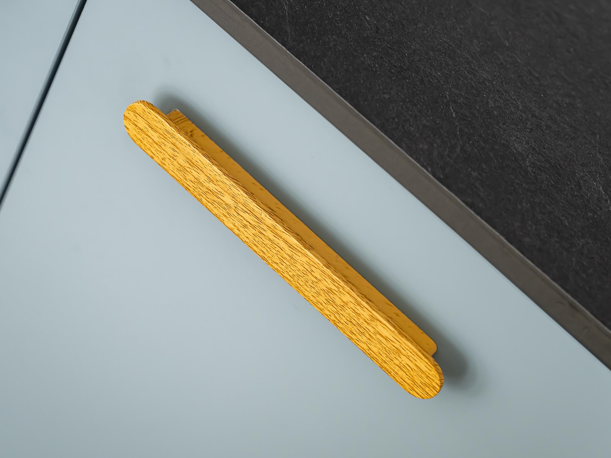 Gros plan sur une porte de placard bleu clair dotée d'une poignée horizontale en bois, à côté d'un plan de travail foncé : un détail élégant dans cet appartement familial haussmannien, où chaque élément témoigne d'une conception soignée et laisse entrevoir la promesse d'une chambre supplémentaire.
