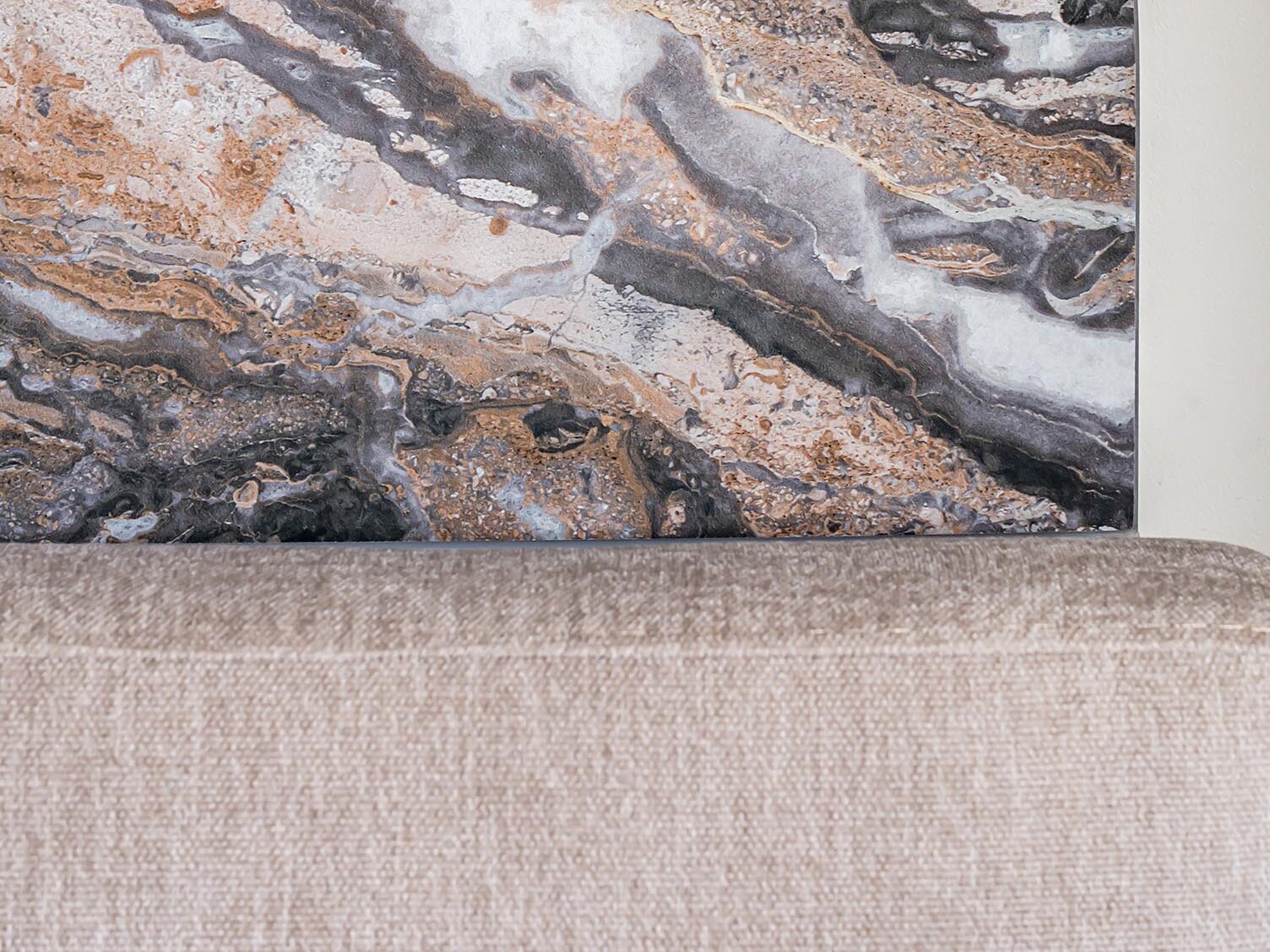 Une tête de lit en marbre brun aux motifs tourbillonnants, placée derrière un canapé ou un lit rembourré beige, sur fond de mur clair : l'idéal pour apporter une touche de style scandinave à votre appartement lors de votre prochaine rénovation.