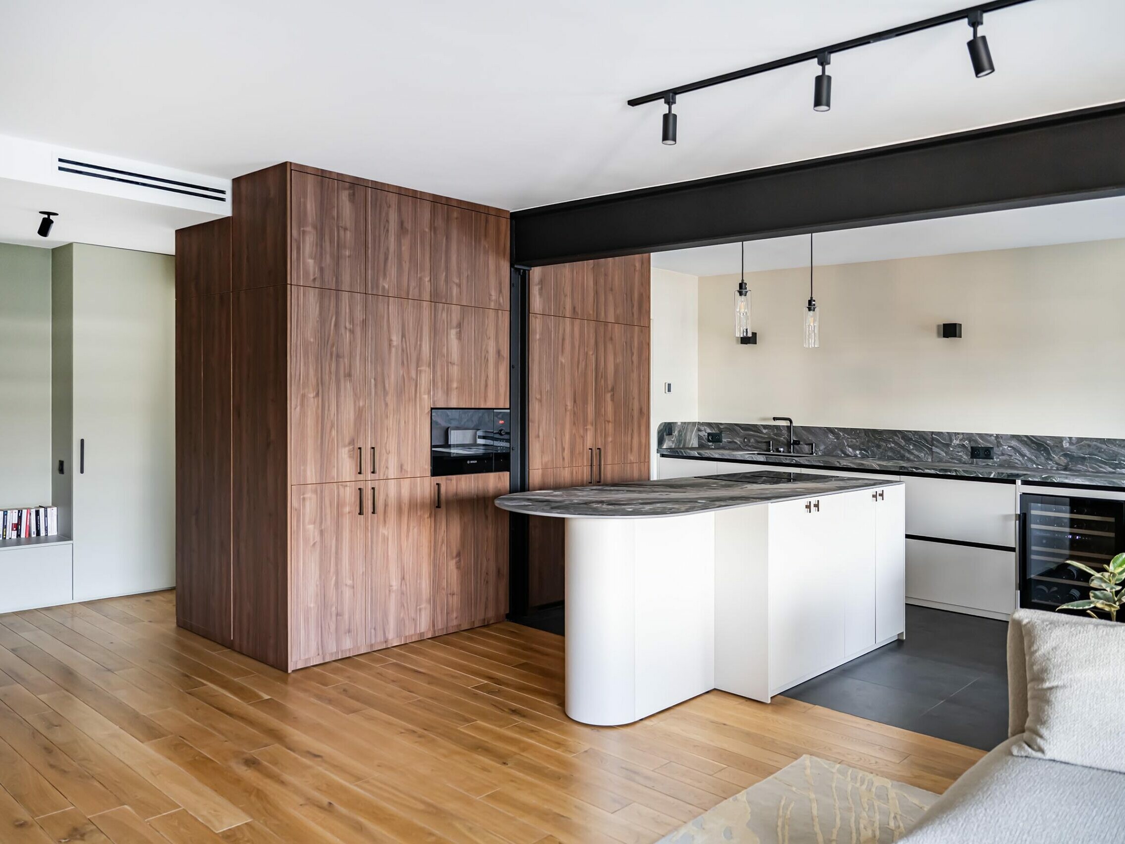 Cuisine moderne avec des placards en bois, des plans de travail en marbre, un îlot, un four encastré, des suspensions et du parquet. Ce design minimaliste se caractérise par des couleurs neutres et un agencement ouvert, idéal pour un appartement d'inspiration scandinave après une rénovation récente.