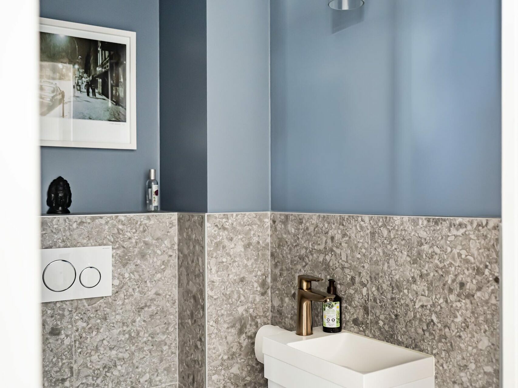 Petite salle de bains moderne équipée d'un WC suspendu, d'un lavabo compact blanc, de murs bleus et gris, d'une suspension et d'une décoration murale encadrée : l'idéal pour un appartement qui cherche à apporter une touche de style scandinave après des travaux de rénovation.