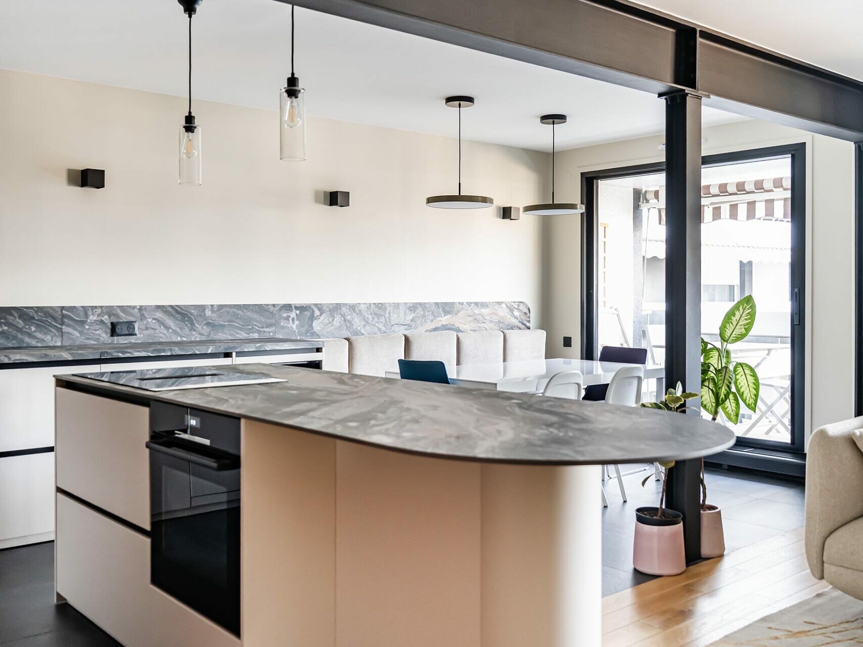 Cuisine moderne dans un appartement de style scandinave, dotée d'un îlot en marbre, d'un four encastré, de suspensions lumineuses et d'un agencement ouvert donnant sur un espace de vie doté de grandes baies vitrées et baigné de lumière naturelle : une rénovation époustouflante qui allie à la perfection élégance et confort.